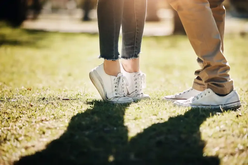 A close-up of two people standing closely together on sunlit grass, capturing the warmth and ease associated with the girlfriend experience.