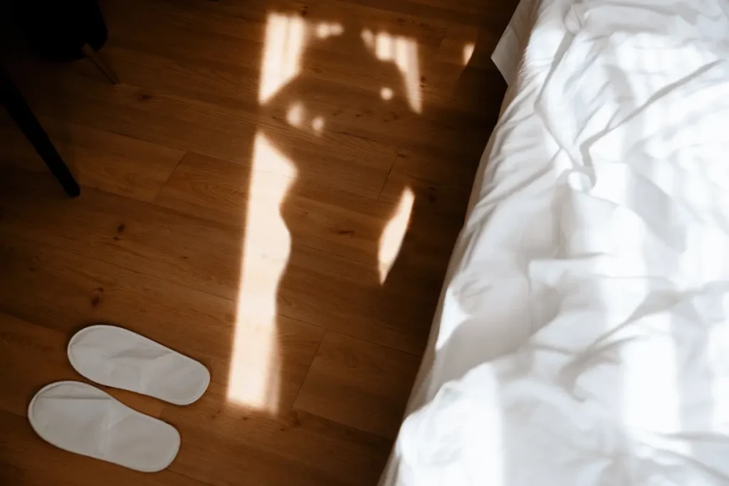 Soft morning light casts a subtle silhouette on a wooden floor beside an unmade bed, evoking privacy and discretion associated with discreet escorts.
