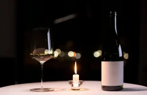 Wine bottle, glass and candlelit table setting, representing the elegance associated with luxury companionship London experiences.