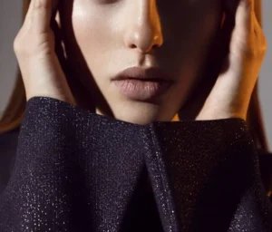 Close-up portrait of a sophisticated older woman wearing a shimmering black top, with her hands gently framing her face.